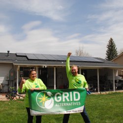 Two people hold up a GRID banner in front of a home with solar panels. 